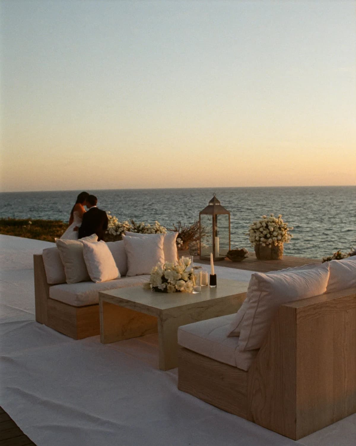 A couple sharing a quiet moment beside an ivory coastal lounge and white flowers at dusk